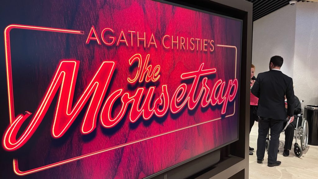 Red sign that says, "Agatha Christie's The Mousetrap" with a patron in a wheelchair next to it
